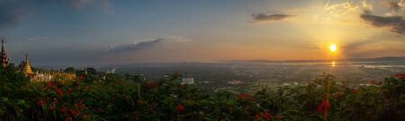 View over the city of Mandalay at sunset from Mandalay Hill, with red flowers and golden pagodas, in Myanmar, formerly called Burmaの写真素材