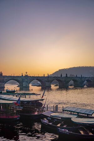 Sunset over the Vltava River in Prague, Czechia, including boats and the silhouettes of statues on the ancient stone Charles Bridgeの写真素材