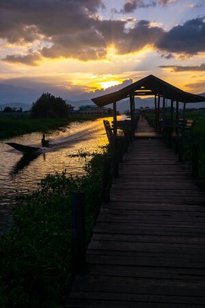 A boat travels down the canal next to the long wooden bridge at Maing Thauk village in Inle Lake in Myanmar (Burma)の写真素材