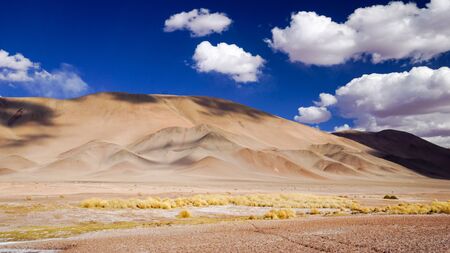 Dramatic clouds cast shadows over yellow hills just outside Tolar Grande in the high altitude puna desert of Salta province in northern Argentinaの写真素材