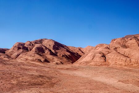 A herd of vicunas pass through the red hills of the Desierto de Laberinto, or Labyrinth Desert, at Tolar Grande in the high altitude altiplano puna desert near Salta in Argentinaの写真素材