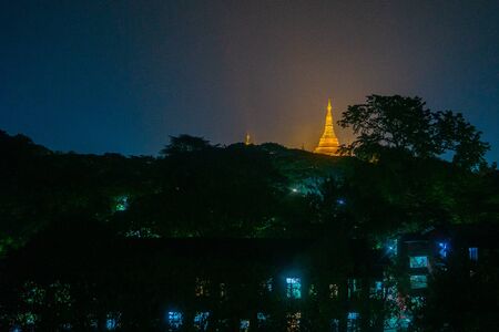 The Shwedagon Pagoda's illuminated golden stupa is visible behind the darkened buildings of Yangon (previously called Rangoon) in Myanmar (Burma)の写真素材