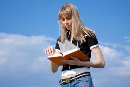 girl standing with book outdoor with sky in backgroundの写真素材