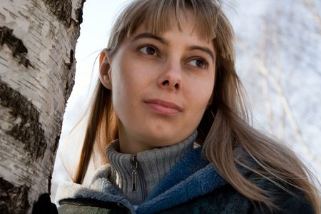 portrait of the beautiful blonde girl standing against the tree in the forest in winterの写真素材