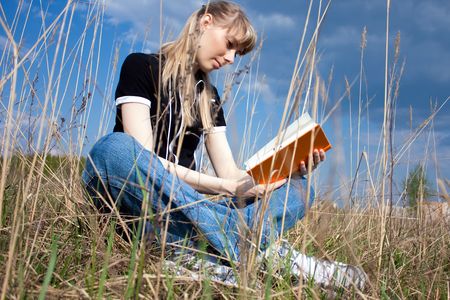 girl reading book and sitting outdoor with sky in backgroundの写真素材