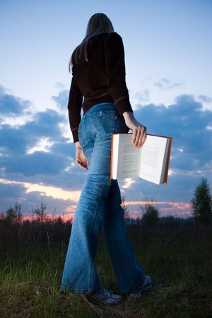girl reading book and sitting outdoor with sky in backgroundの写真素材