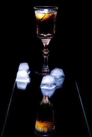 photo of still life with goblet  of alcohol and ice with reflections isolated on dark backgroundの写真素材