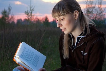 girl reading book and sitting outdoor under the tree with sky in backgroundの写真素材