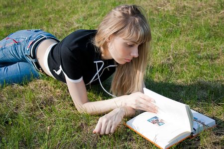 girl reading book and lying on green grassの写真素材