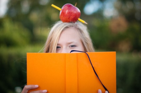 beautiful young student girl standing in park with opened book in her hands and red apple on her head (focus on book)の写真素材