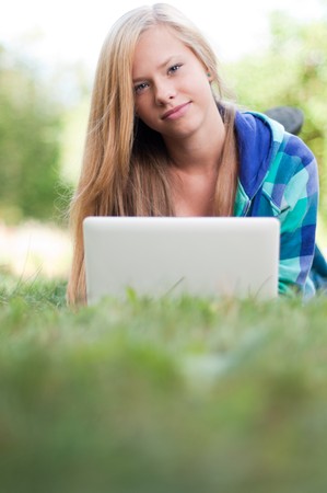 beautiful young student girl lying on grass with laptop, looking into the camera and smilingの写真素材