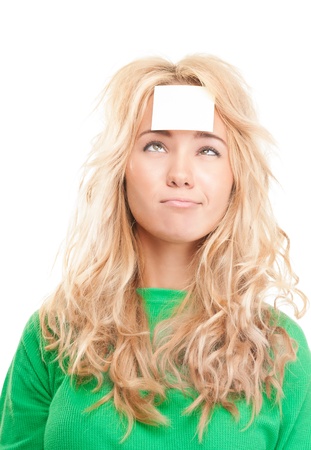Beautiful and pensive young woman thinking. Isolated on white background. Looking up at the blank sticky note on her forehead.の写真素材