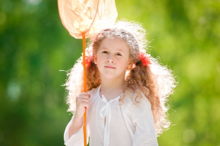 beautiful little and happy girl standing with butterfly net, smiling and looking into the camera. Summer park in background.の写真素材
