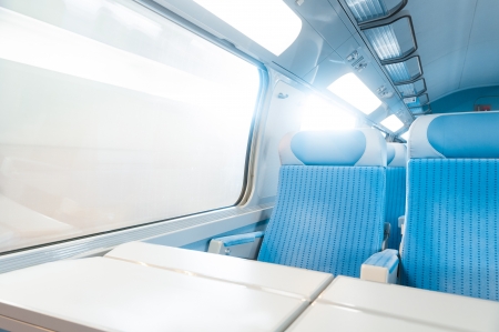 Inside cabin of modern express train. Nobody in blue chairs at window. Motion blur. Comfortable chairs and table in foreground, sun in background. Travel, France, Europe.のeditorial素材