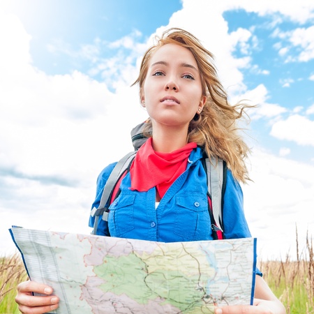 Young pretty woman tourist standing in wheat field with map  Blue cloudy sky in background behind...