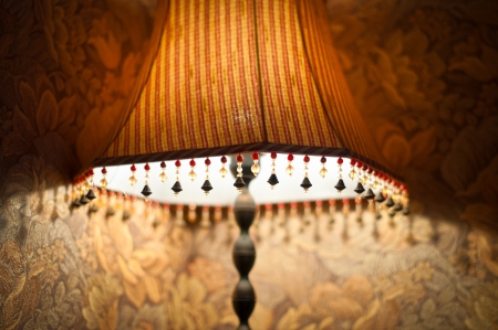 Classic vintage lamp with yellow and brown striped shade giving dim light in evening  Retro lamp decorated with beads stands near wall  Home interior and design の写真素材