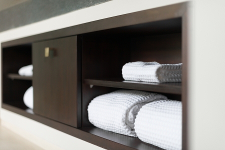 Wall with built in wooden shelf  Neat stack of white soft towels in bathroom  Closet with clean folded textile for spa and hygiene  Modern interior of hotel room  Luxury resort with classic design の写真素材