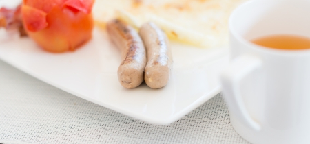 Close up view of tasty and simple breakfast with tomato, sausages and tea  Breakfast served on white plate and tablecloth  Delicious food and meal の写真素材