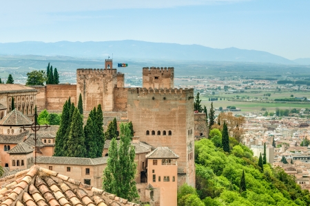 Scenic view of medieval fortress in Alhambra, Spain. Background of blue sky, hills and town. Ancient building surrounded by green trees and bushes. Travelling and tourism. Architecture of Europe.のeditorial素材
