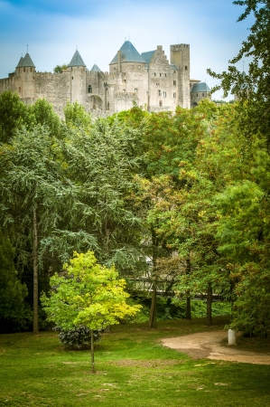 Historic Fortified City of Carcassonne in France towering over green alley with curved path. Medieval fortress under clear blue sky with greenery in foreground. Architecture and landmarks of Europe.のeditorial素材