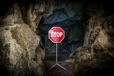 Entry to dangerous cave blocked with red and white Stop sign. Warning about danger on way to dark...