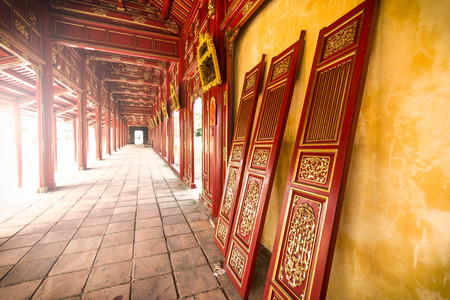 Beautiful red wooden hall with golden ornate details in Hue citadel, Vietnam, Asia. Vanishing roof and tiled floor. Sunlight through columns. Famous destination for tourists. UNESCO Heritage site.の写真素材