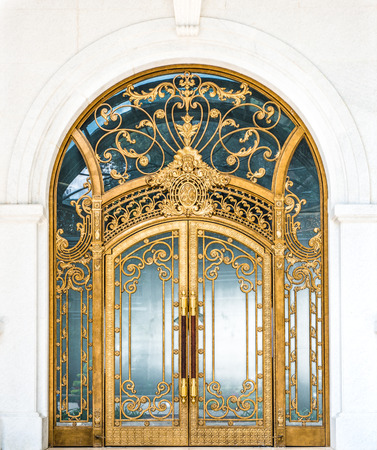 Beautiful arched doorway. Door made of wood, gold and glass reflecting arch. White wall of building with elegant gilded entrance. Old style of door with golden ornate details. Tourist attraction.の写真素材