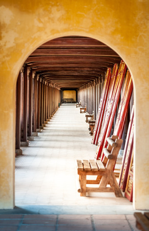 Arched doorway of Hue citadel, Vietnam, Asia. Yellow stone wall with entrance to hall. Wooden benches along wall, red ceiling and columns. Famous destination for tourists. UNESCO Heritage site.の写真素材