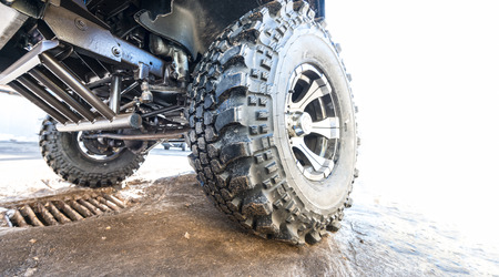 Offroad vehicle tires closeup. Vehicle on dirty pavement. Underside view of car. Big wheels for...