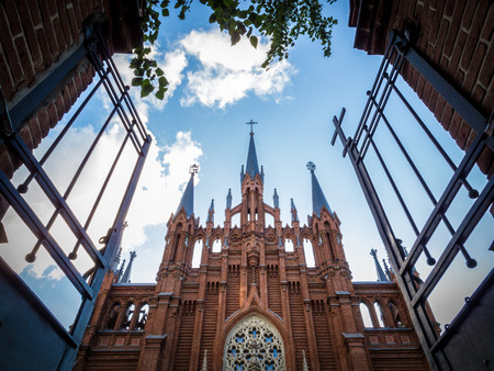 Open metallic gate towards an old Christian church with impressive architecture, under a cloudy blue sky, concept of salvation, heaven and spiritual comfort, from low-angle.の写真素材