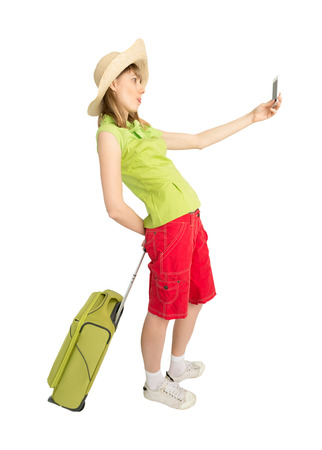 Happy lady tourist in red shorts green blouse and straw hat with bag makes picture by phone. Isolated on white background. Traveler has Interesting trip on summer vacation.の写真素材