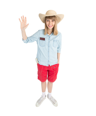 Happy lady tourist in blue shirt red shorts and straw hat. Girl going to travel. Isolated on white background. Interesting trip on summer vacation. Woman greeting to somebody.の写真素材