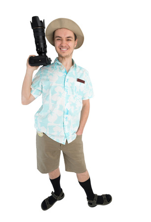 Happy man tourist in blue shirt, brown shorts and hat holds dslr camera. Traveler smiles and going to photo tour. Isolated on white background. Interesting trip on summer vacation.の写真素材