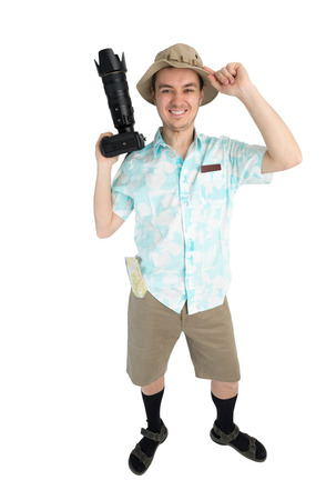 Happy man tourist in blue shirt, brown shorts and hat holds dslr camera. Traveler smiles and going to photo tour. Isolated on white background. Interesting trip on summer vacation.の写真素材
