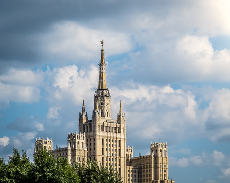 One of Moscow's famous highrises. Blue cloudy sky in background, tree in foreground. Summer in...
