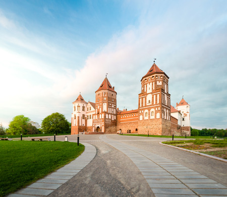 Green trees and gras and blue sky at sunny day. Stone road to beautiful Mir castle in Belarus. Medieval fort became sight for tourists.のeditorial素材