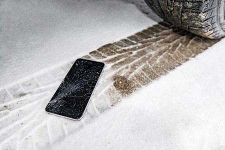 Phone with broken screen on snow in car trail. Glass covered with snow flakes. Device run over by wheel.の写真素材