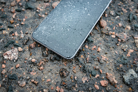 Phone with broken screen on asphalt. Someone dropped device. Glass covered with snow flakes.の写真素材