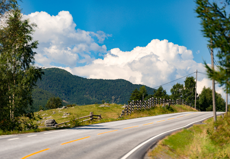 Empty winding country road in Norway, Europe, Scandinavia. Auto travel on sunset. Blue sky with clouds.の写真素材