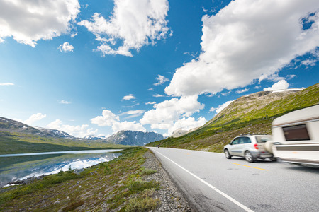 Car with RV trailer in mountains of Norway, Europe. Auto travel through scandinavia. Blue cloudy sky and lake in background.の写真素材