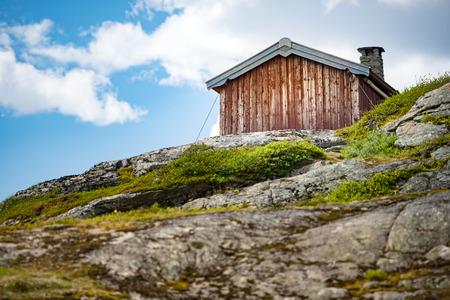 Wooden house high in mountains of Norway, Scandinavia, Europe. Blue cloudy sky in background, rocks in foreground.の写真素材