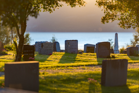 Cemetery in Norway on sunny day with blue water and mountain in background and green grass in foregroundのeditorial素材