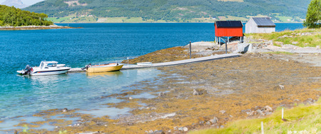 Beautiful landscape of Norway. Red barn, trees and water, mountains in background. Travel in Scandinavia, Europe. Boats at pier.の写真素材