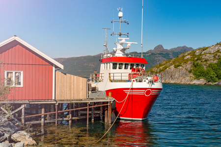Tugboat or fishing boat at pier, Norway, Europe. Ship in foreground and blue sky and mountains in background. Scandinavia travel.の写真素材