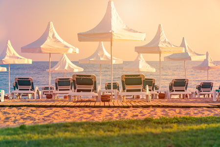Beach in Turkey with green grass in foreground, white sun shade umbrellas sea and sunset sky in backgroundのeditorial素材