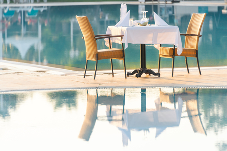 Chairs and table near pool at hotel restaurant. Cutlery and napkings on tables. Resort life on holidays.のeditorial素材