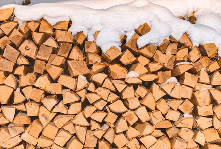 Stack of wood logs. Preparation of firewood for the winter. Pile of chopped lumber covered with snow.の写真素材