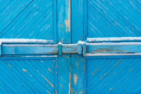 Wooden gate covered with white snow. Blue colored pattern of planks. Door closed on old bolt.の写真素材