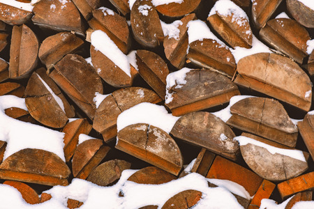 Stack of wood logs. Preparation of firewood for the winter. Pile of chopped lumber covered with snow.の写真素材