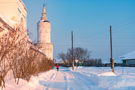 Monastery wall with tower at winter. Blue cloudy sky, road covered with snow. Sunset sun shining on old walls.の写真素材